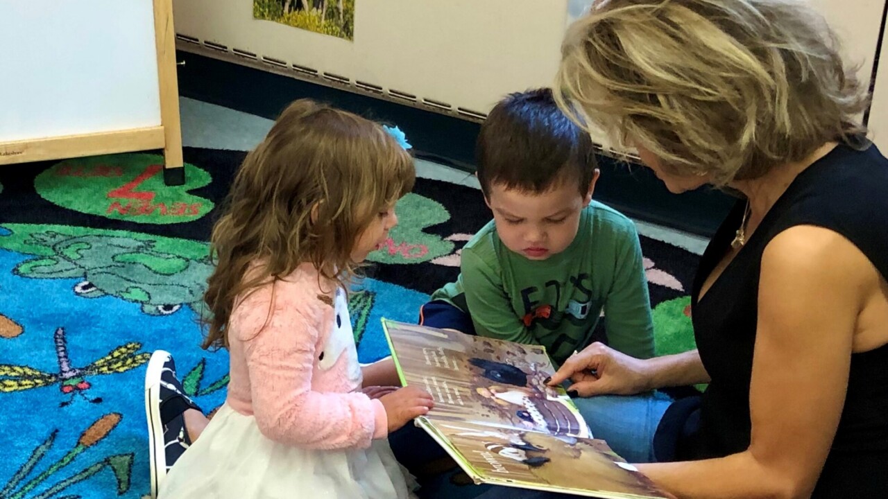 An instructor reading a book to two children on the floor.