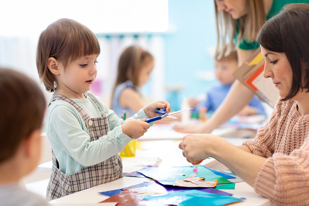 A girl holding a pair of scissors while she crafts with an instructor.