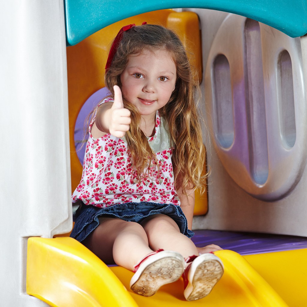 A little girl on a slide giving a thumbs up.