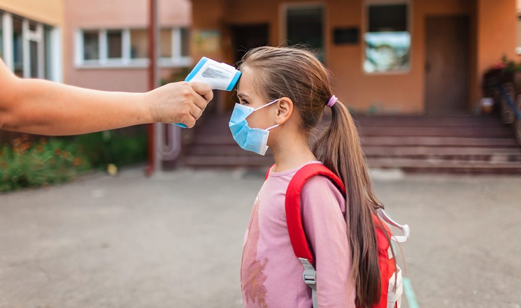 A little girls wearing a mask getting her temperature taken.