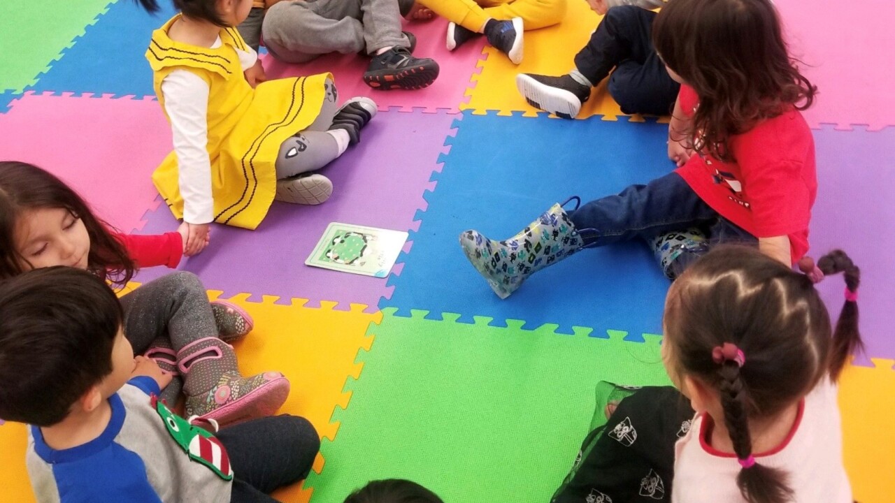 A group of children sitting in a circle holding hands on a colorful foam mat.